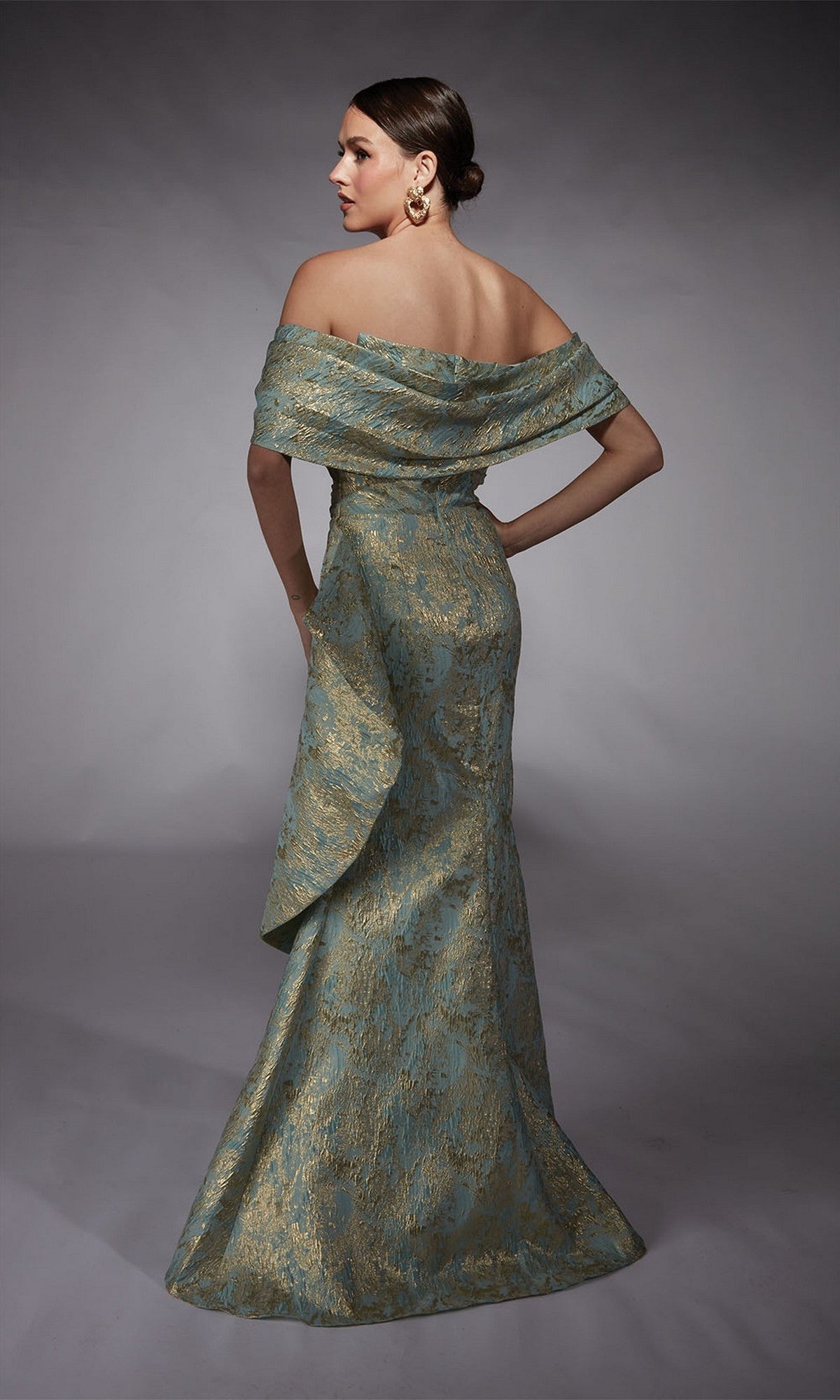 A woman stands facing away in a studio wearing the Alyce 27750 long formal dress, featuring a strapless metallic jacquard brocade design and mermaid skirt.
